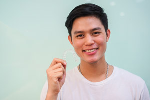 Young male holding clear aligner in hand. Lewis Family & Implant dentistry provides Invisalign to patients in Vancouver WA.