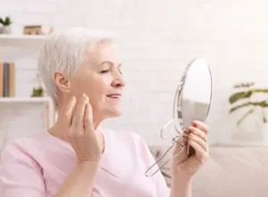 woman smiles in the mirror as she realizes dentures are easy to wear