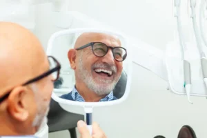 Senior man admiring his new smile in a dental clinic while holding a mirror